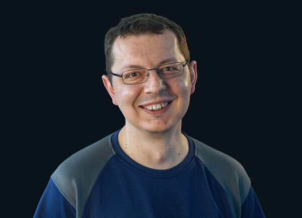 Ivica Stevic, employé de la production de couleur, pose avec un sourire devant un fond noir avec un T-shirt Schaffner GF AG.