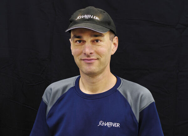 Markus Gubisch, employé dans le domaine de la logistique, pose sur un fond noir avec un polo Schaffner GF AG et une casquette Schaffner.