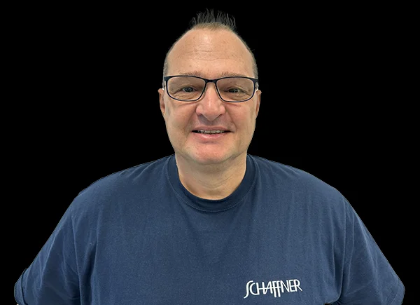 Marcus Widmer, Mitarbeiter der Farbproduktion, posiert lächelnd vor einem schwarzen Hintergrund im Schaffner GF AG-Shirt.