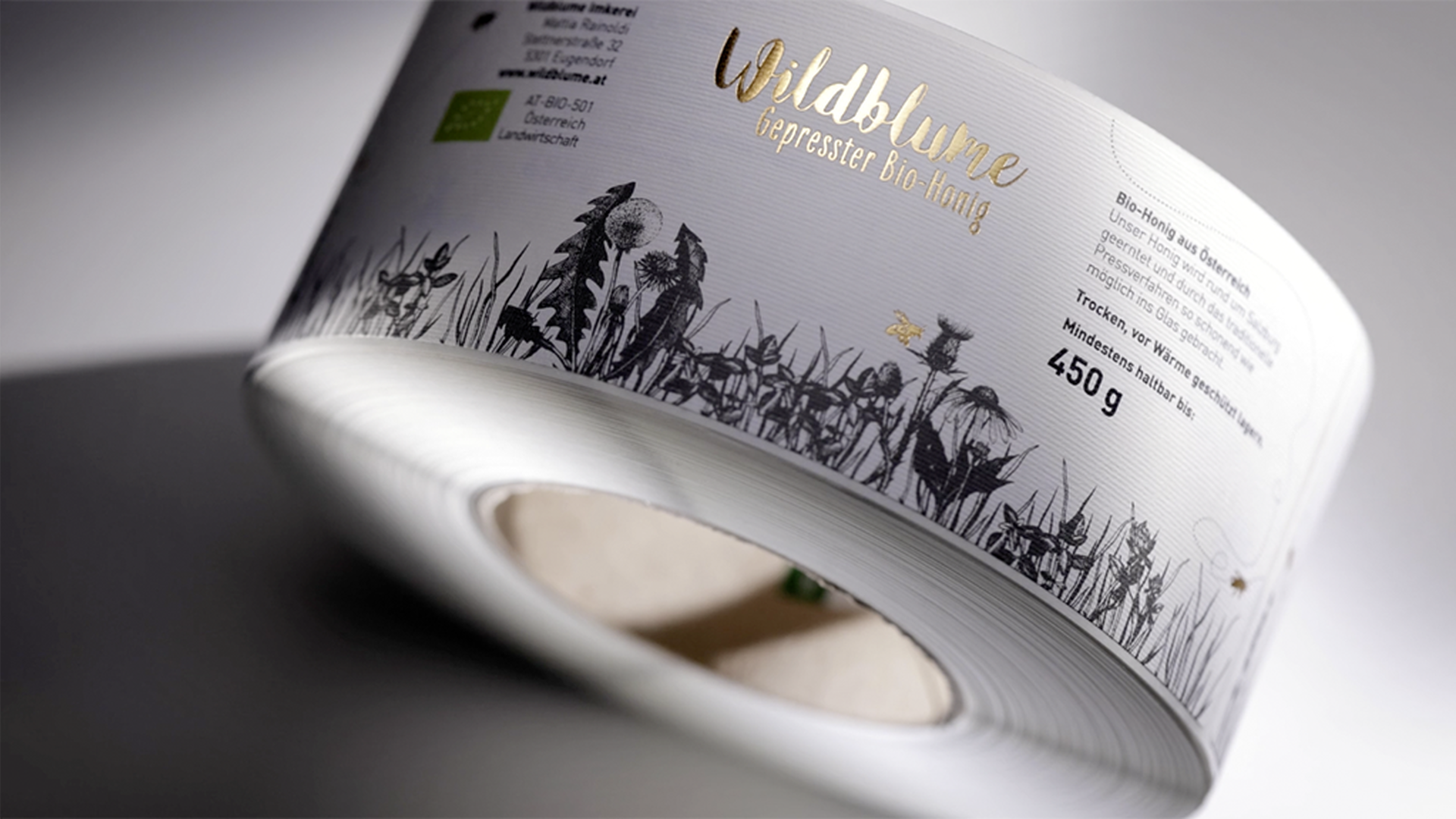Rolle mit Etiketten „Wildblume Bio-Honig“ mit goldener Schrift und floraler Illustration auf weißem Hintergrund.