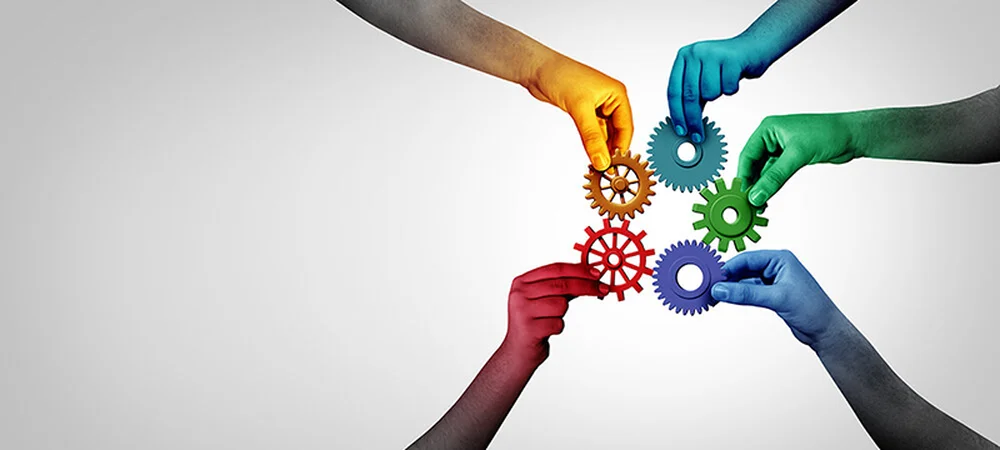 Farbige Hände fügen Zahnräder zusammen – Symbolbild für Teamarbeit, Vielfalt und Zusammenarbeit bei Schaffner GF AG.